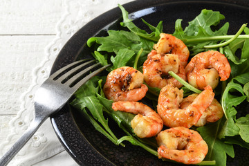 fried prawns or shrimps on arugula rocket salad with lemon and bread served on a black plate, white...