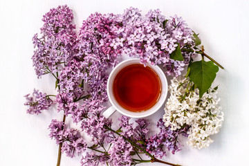 Obraz na płótnie Canvas Cup of black tea with a bouquet of lilac on a white table
