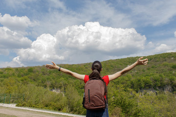 Young hiker girl with backpack enjoying and looking to the sky with clouds
