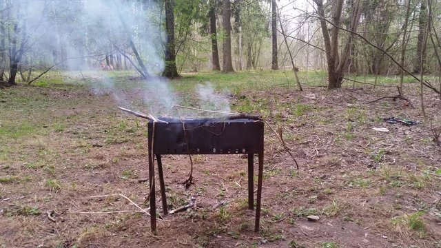 Rusty metal brazier for frying meat smokes in the forest
