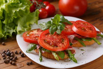 Two toast with asparagus, ham, tomato  and basil on a white plate, close-up.
