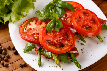 Two toast with asparagus, ham, tomato  and basil on a white plate, close-up.