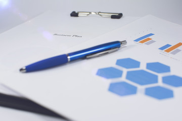Clipboard with a white piece of paper and charts with blue pen on white background. Technology and business concept. Lens flare in the background.
