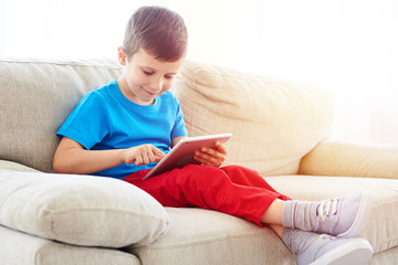 Small boy looking and touching a screen of a tablet