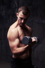 Male with torso demonstrating muscles while doing exercises with dumbbell