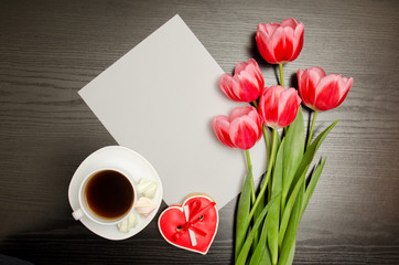Fototapeta na wymiar Clean sheet of paper, pink tulips and a mug of coffee. Black table. top view