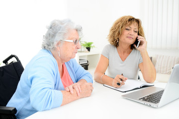 mature woman helping assisted elderly senior female with administrative procedures and paperwork on internet with a laptop computer at home - obrazy, fototapety, plakaty