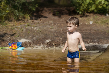 little boy in blue suit walks into the water of a lake on a summer day