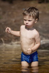 Fototapeta na wymiar little boy in blue suit walks into the water of a lake on a summer day