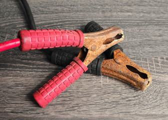 Jumper cables to recharge the car battery. Red and black, negative and positive cable on a wooden background.