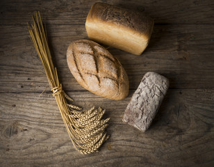 Bread border on wood with copy space background. Brown and white whole grain loaves still life composition with wheat ears scattered around. Bakery and grocery food store concept.