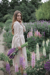 Young attractive teenager girl in long vintage dress dream and walk in park among the lupine flowers. Simple life and ecology style fashion clothes concept