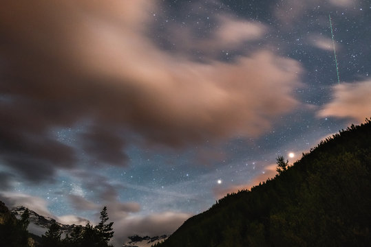 The starry sky with blurred motion colorful clouds and bright moonlight. Expansive night landscape in the European Alps, fisheye ultra wide view.
