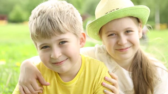  The children are looking at the camera. The smiling sister hugs her brother. 