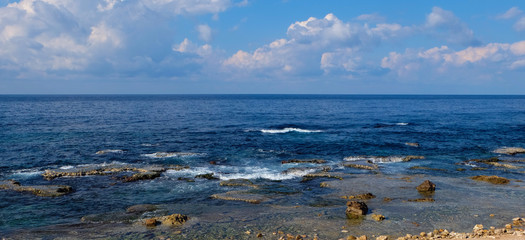 seascape panorama - natural rock formations at the coast and clear blue water with light waves to the horizon