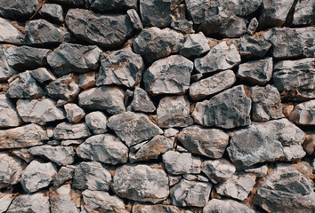 old stone wall consisting of stacked naturally shaped loose rocks - background pattern