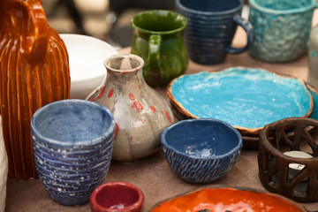 Lots of handmade tableware - ceramic cups, plates at pottery shop. Colorful blue and orange clayware background