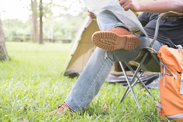 man tourist sitting on chair and reading map in front of tent at camping site in forest. Outdoor activity in summer. Adventure traveling in national park.