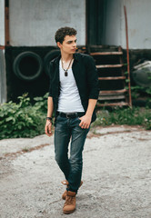 A young guy is walking along the street. Poses for men's photo sessions. Beautiful appearance, clothes in rock style.