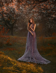 Blonde girl walking in the garden at sunset. She wears a luxurious purple dress.
