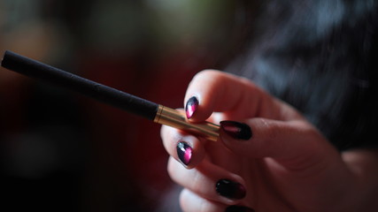 Black cigarette with golden filter in woman's hand