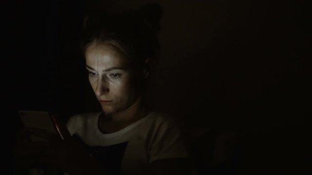 Tired sad woman using cellphone at night.