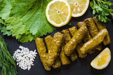 Foto op Plexiglas Delicious stuffed grape leaves (the traditional dolma of the mediterranean cuisine) on black dish with leaves, lemon slices, rice, parsley and dill © dinosmichail