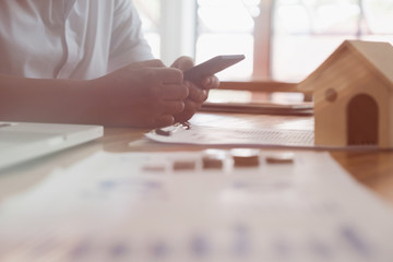Businessman using smart phone with money coin and accounting graph and chart and house model on table at office. growth of financial income from investment. Property tax, loan for real estate concept