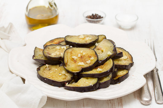 fried eggplant with garlic on white plate on wooden background