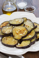 fried eggplant with garlic on white plate on wooden background