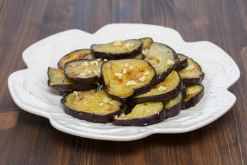 fried eggplant with garlic on white plate on wooden background