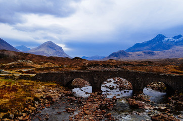 isle of skye landscape, mountain with snowy top and small stone bridge.