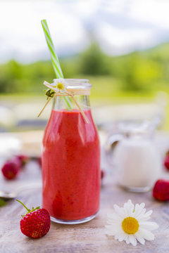 Delicious strawberry smoothie on the wooden table in the garden.