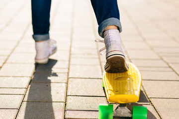 Close up of slim lady in jeans and white sneakers ready to ride her penny board skateboard in sunset light. Modern urban hipster girl have fun. Good sunny summer day for skateboarding and have fun.