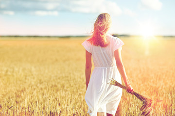 young woman with cereal spikelets walking on field