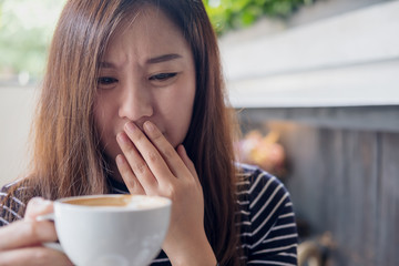 Closeup image of Asian woman holding hot coffee with feeling strange and smelling bad in coffee shop