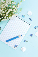 A bouquet of lilies of the valley, a notepad and a pencil lie on a blue wooden table