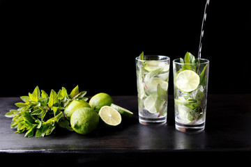 Mojito traditional beach refreshing cocktail alcohol drink in glass bar preparation pouring soda water, lime, mint leaves, sugar, and rum