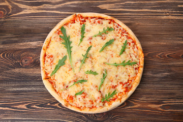 Delicious pizza with melted cheese and rocket salad on wooden table