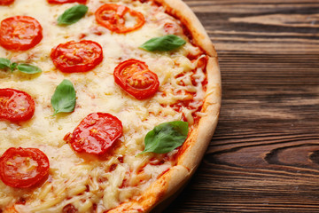 Delicious pizza with tomatoes, basil and melted cheese on wooden background