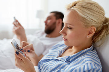 couple with smartphones in bed at home