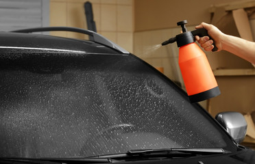 Worker spraying water onto car window prior to tinting
