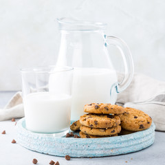 Stack of chocolate chip cookies on blue stone plate with glass of milk on light gray background. Selective focus. Copy space.