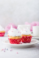 Vanilla cupcakes with white frosting cream and pink sprinkles on light gray background. Birthday party food concept. Copy space.