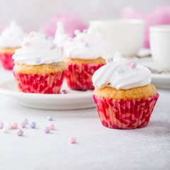 Vanilla cupcakes with white frosting cream and pink sprinkles on light gray background. Birthday party food concept. Copy space.