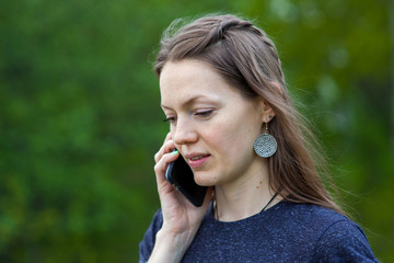 smiling girl speaks by mobile phone against summer green nature.