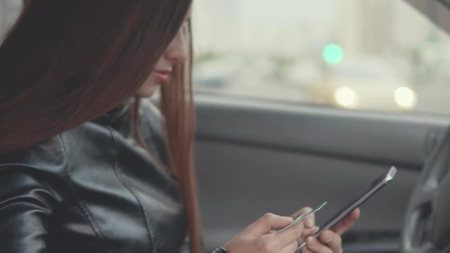 Young attractive woman is making an online purchase in the car via mobile phone and electronic card