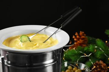 Cucumber slice dipped into cheese fondue on black background
