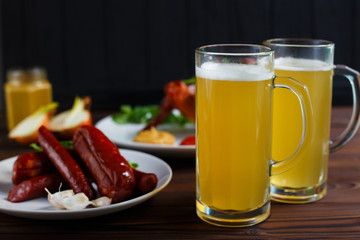 Two mugs of lager beer with crusty grilled chicken wings and various sausages