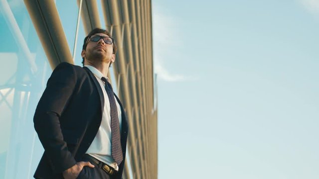 Portrait of worried businessman standing outside the office building, waiting car, looking at the watch. Close up